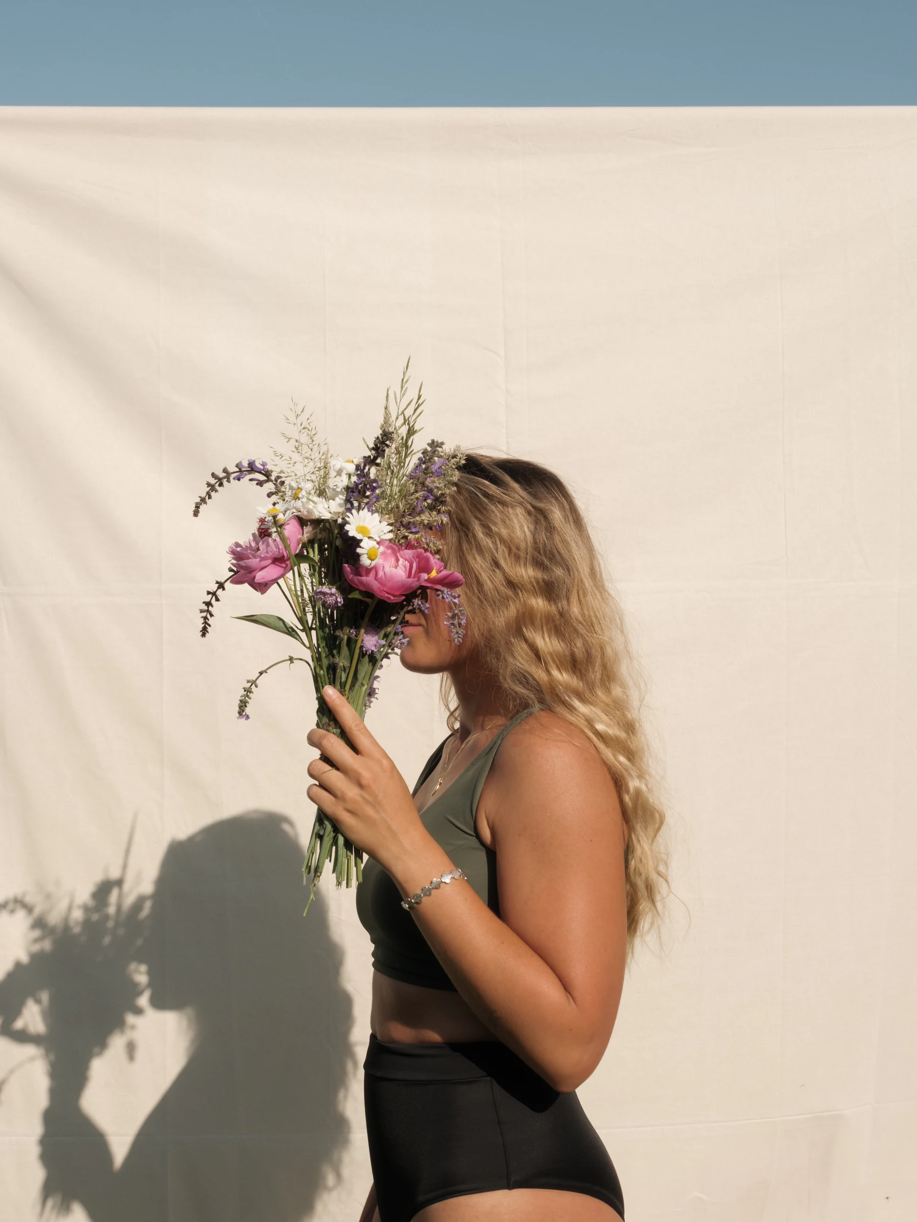 Woman holding a bouquet of wildflowers in front of a pale fabric backdrop